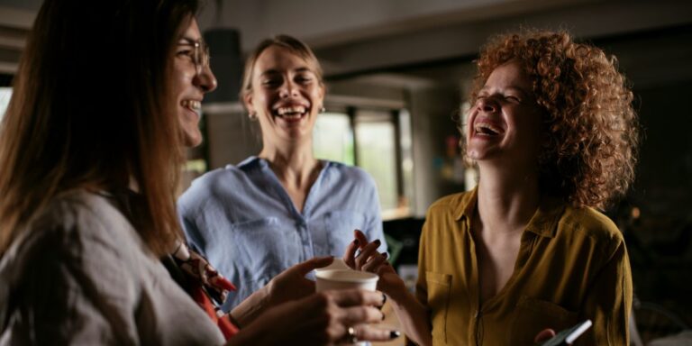 Two female colleagues laughing during a coffee break in office